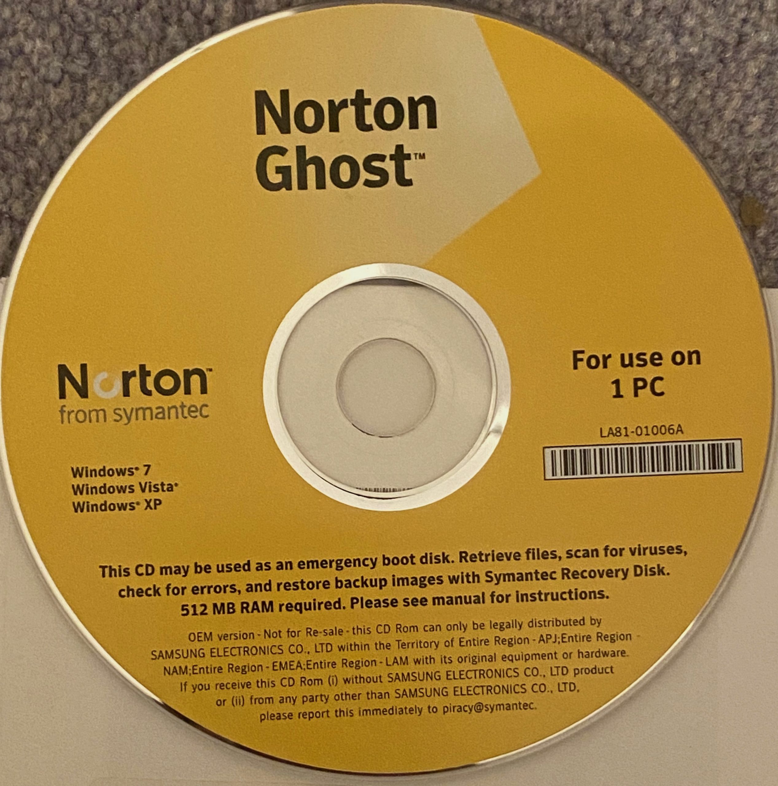 A yellow Symantec Ghost CD labeled "For use on 1 PC," compatible with Windows 7, Vista, and XP. It includes instructions and requirements for use as an emergency boot disk. The CD rests on a light gray textured surface.